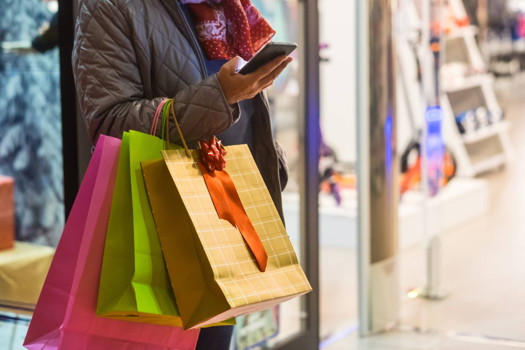 One people alone. A senior woman enjoys evening shopping while taking advantage of offers and discounts. On his arm a lot of shopping bags while she looks at her cell phone One people alone. A senior woman enjoys evening shopping while taking advantage of offers and discounts. On his arm a lot of shopping bags while she looks at her cell phone