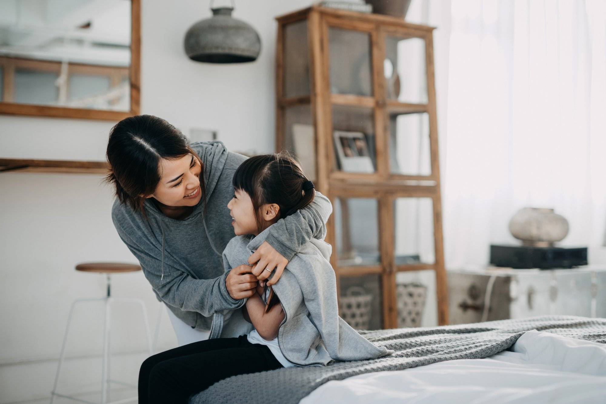 Caring young Asian mother putting a coat on her daughter at home Caring young Asian mother putting a coat on her daughter at home